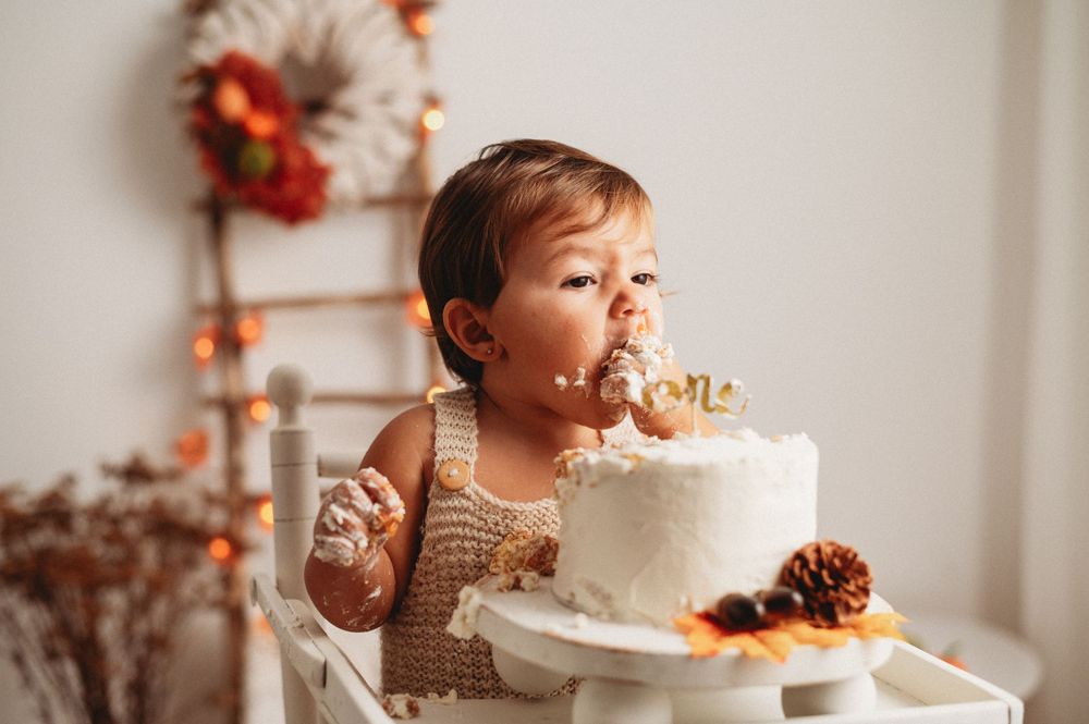 Child enjoying a white frosted cake adorned with pinecones and autumn decorations.
