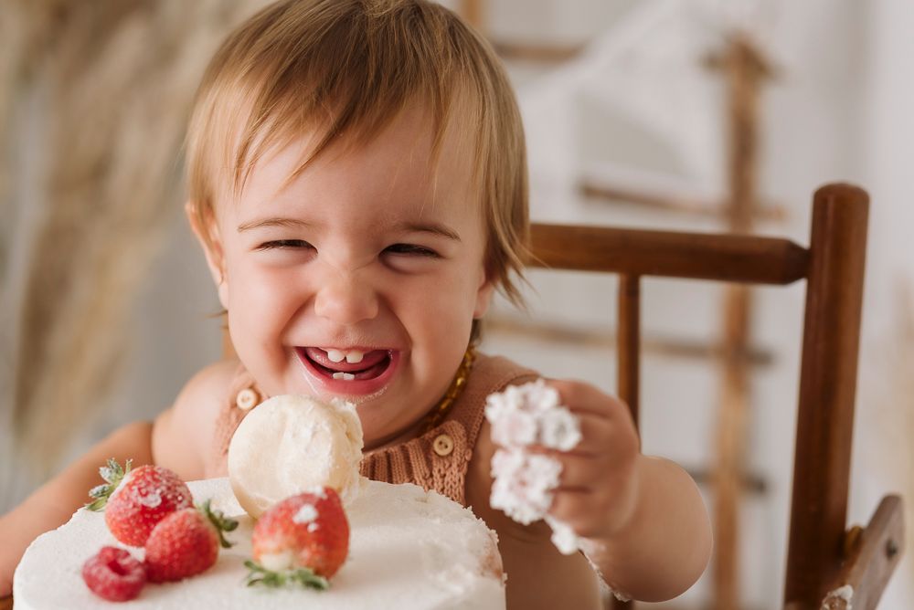 Happy toddler eating cake with strawberries and whipped cream, showing pure joy.