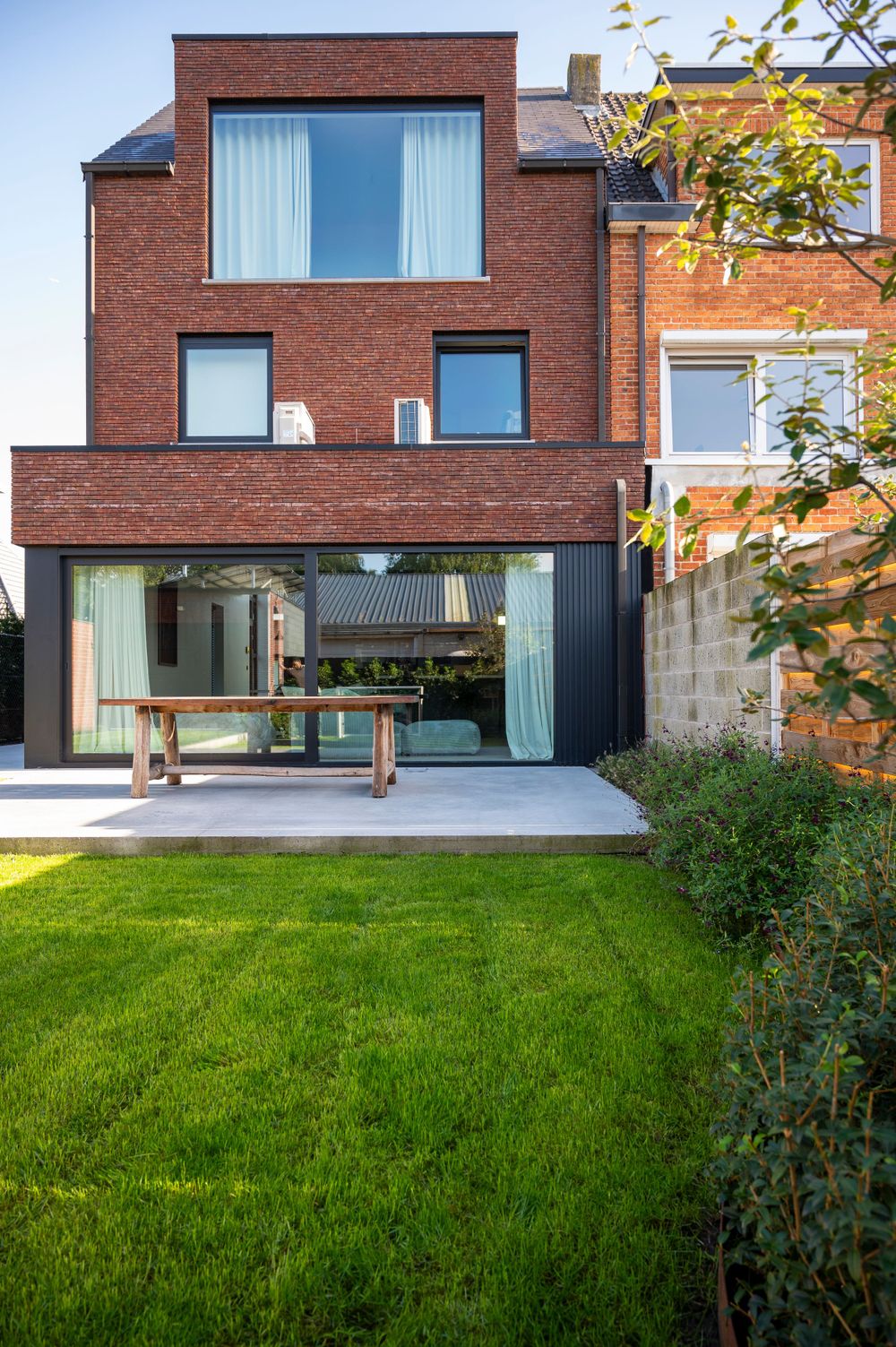 Modern brick house with large windows and manicured green lawn in front.