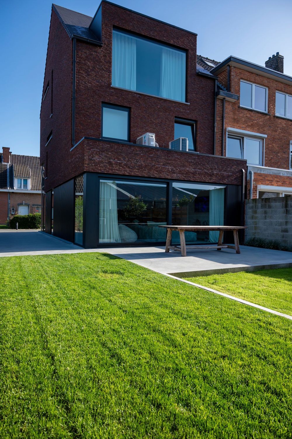 Modern brick house with angular architecture features a sloping green lawn and large glass windows.