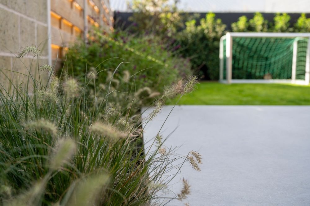 Ornamental grasses sway in front of a soccer goal on a green lawn.