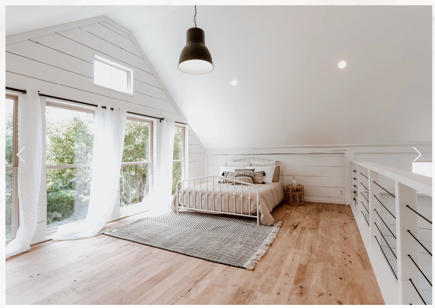 Modern loft space with white walls, hardwood floors and large windows providing natural light.