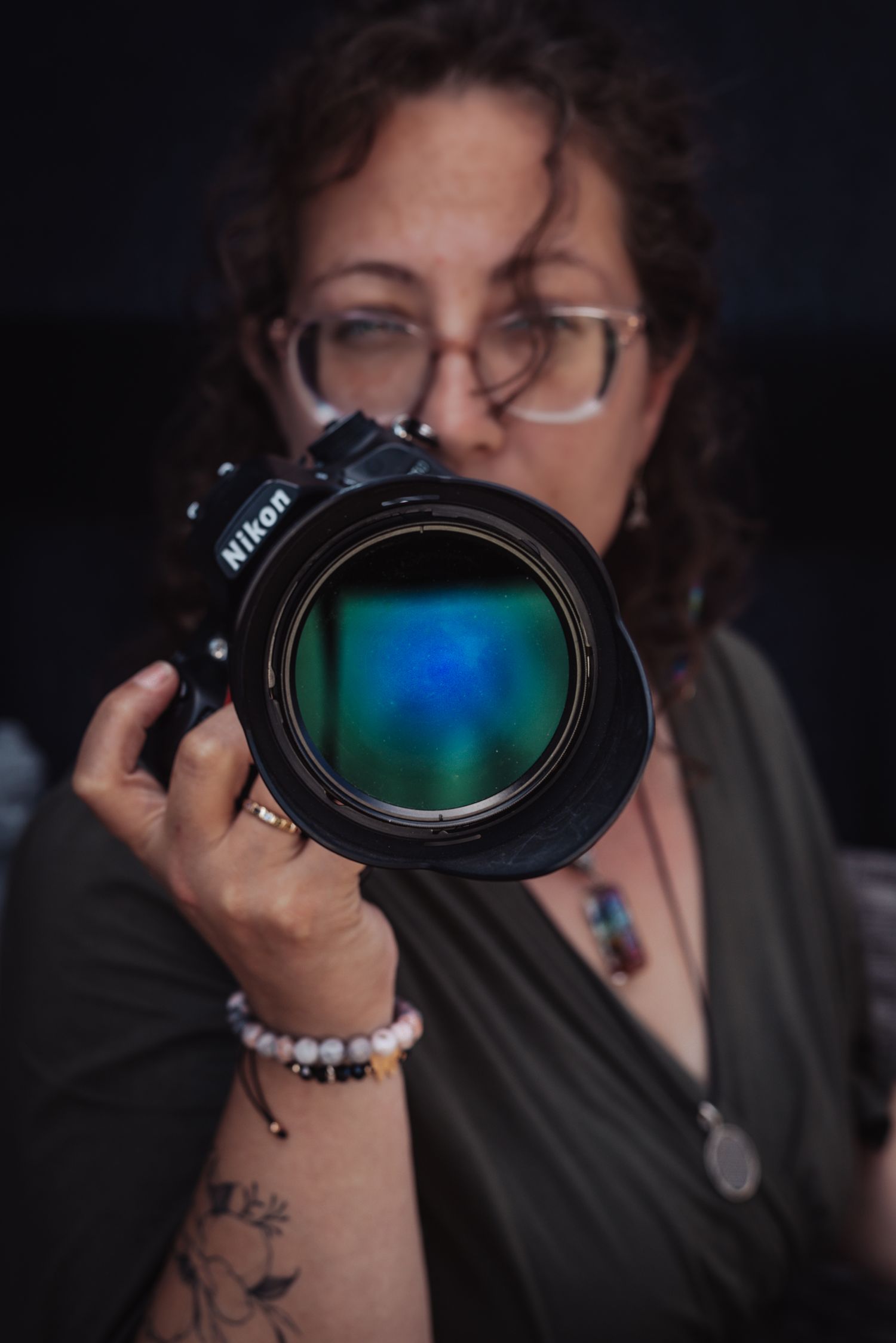 Close-up of a Nikon camera lens being held with colorful reflection visible.