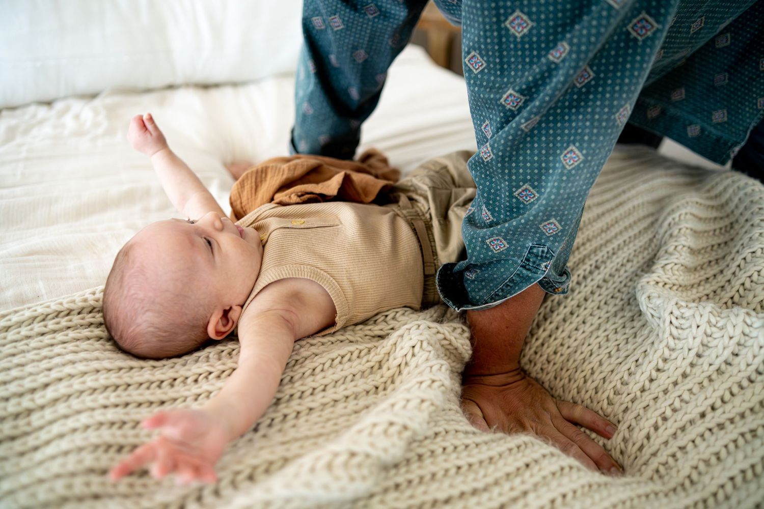 Baby in tan outfit lies on textured knit blanket during intimate family photoshoot.