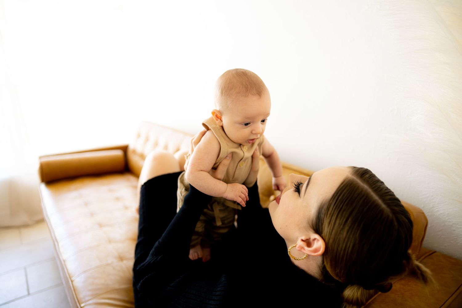 Parent and baby share playful cuddles on beige blanket.