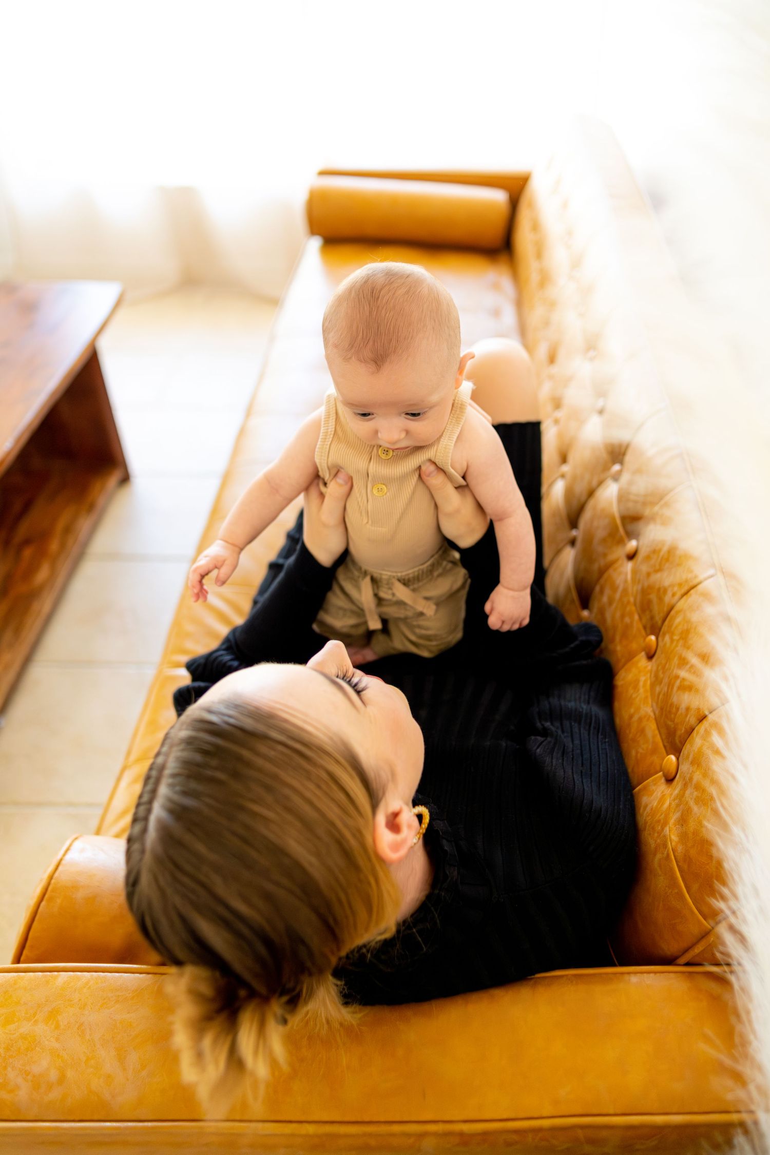 Parent and baby share a tender moment playing together on a vintage orange leather couch.