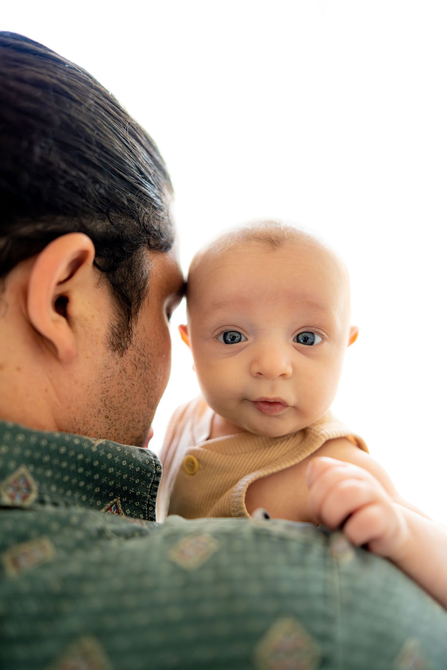 Baby with bright blue eyes gazes intently during tender moment with parent.