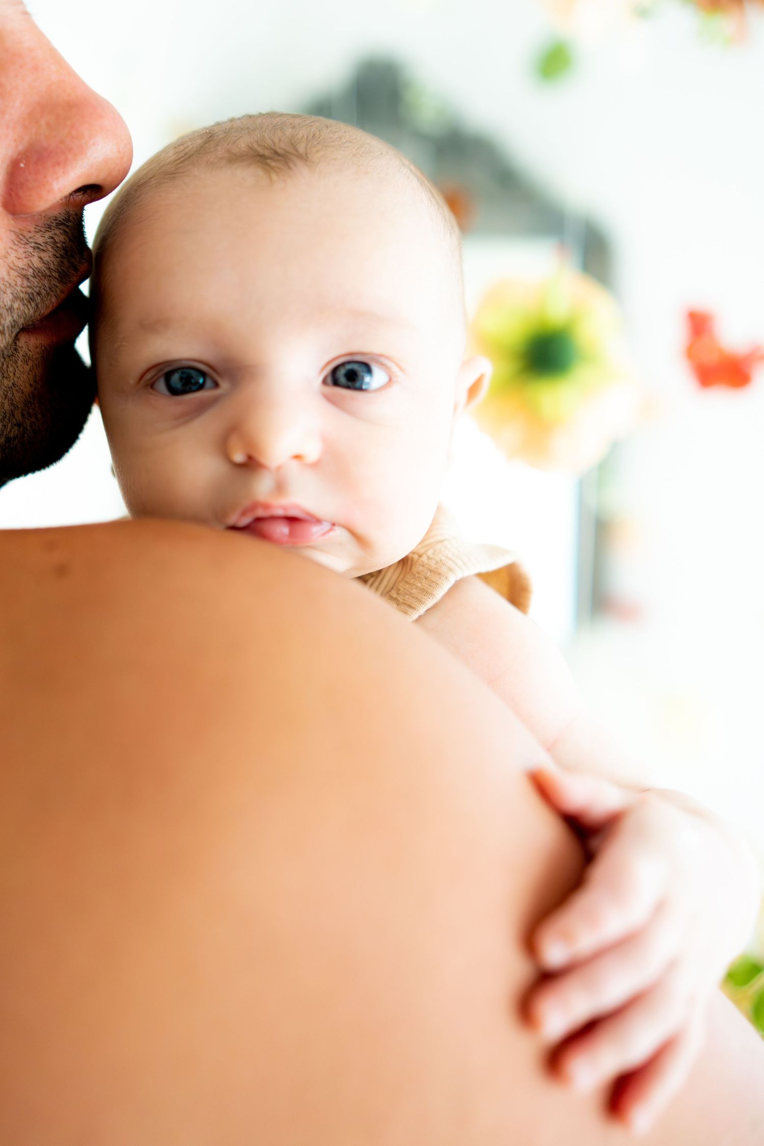 Close-up of a baby with bright blue eyes being held against a shoulder.