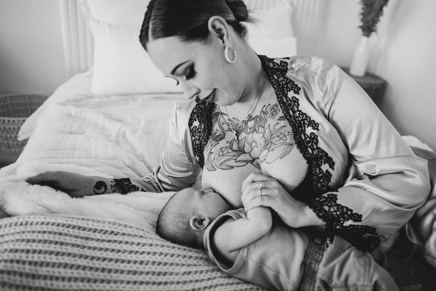 Intimate black and white photo of nursing baby in bed with lace-robed parent.