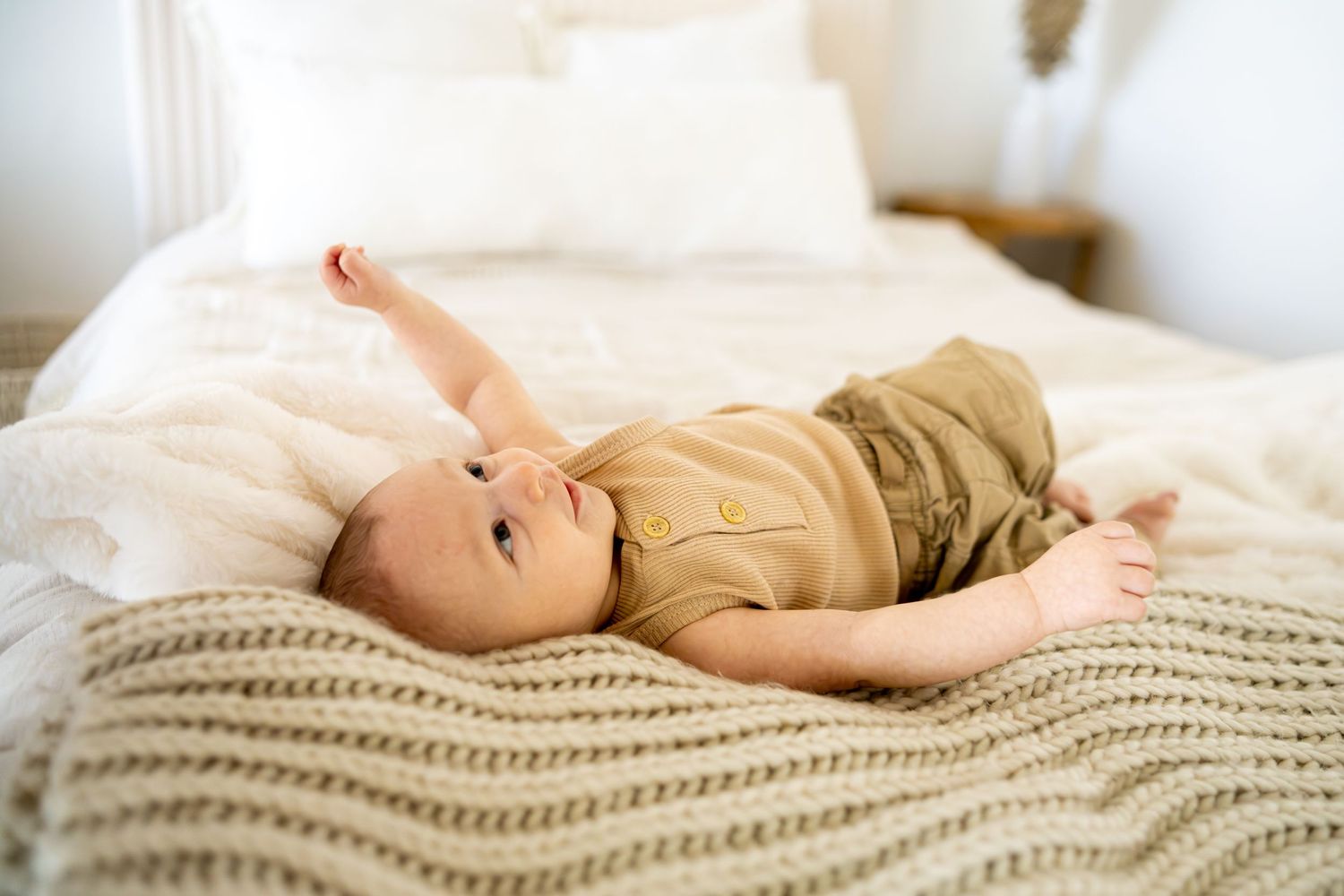 Baby lying contentedly alone on textured cream knit blanket.