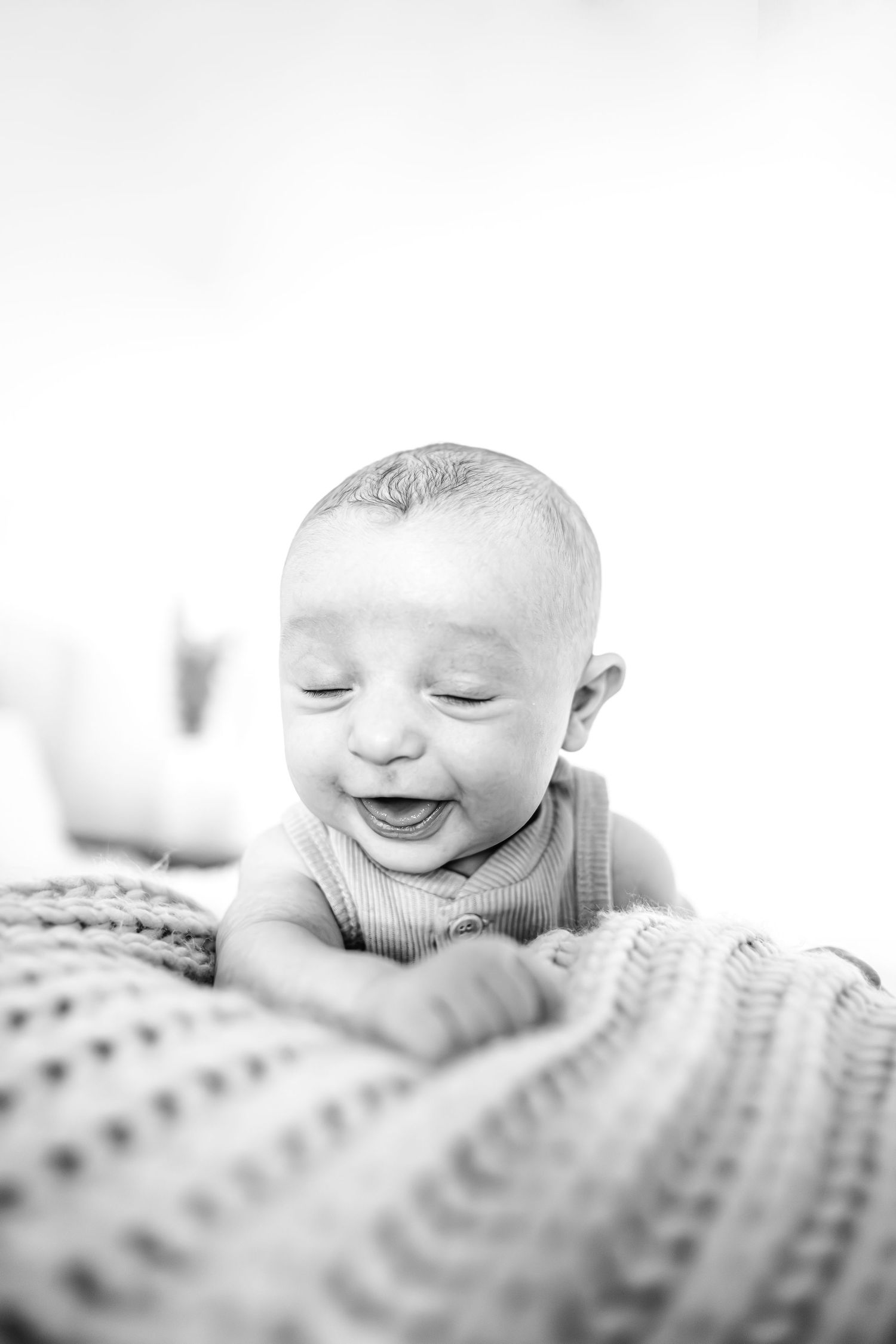 Black and white portrait of a smiling baby lying on a patterned blanket.
