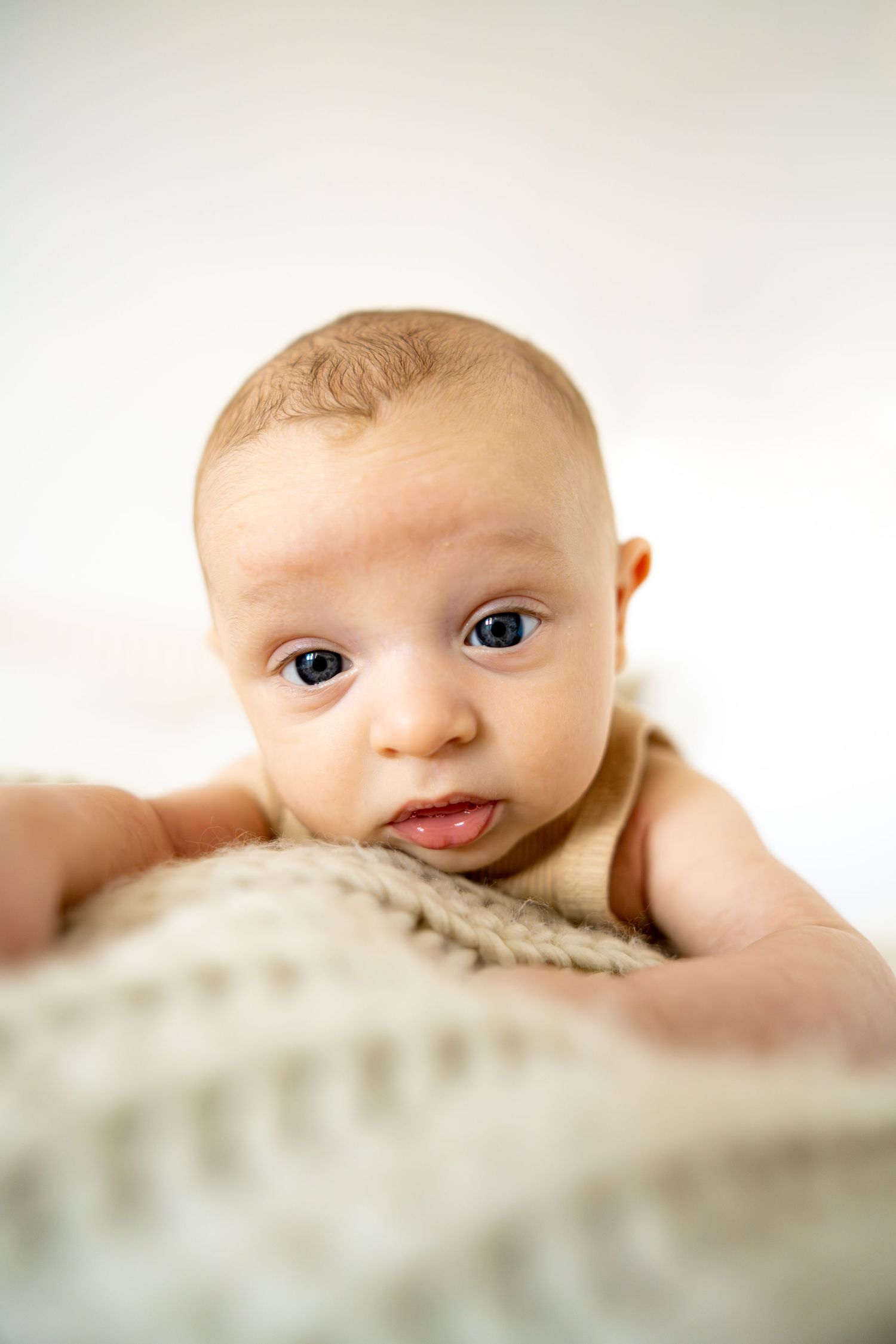 Close up of baby with curious expression lying on textured fabric.
