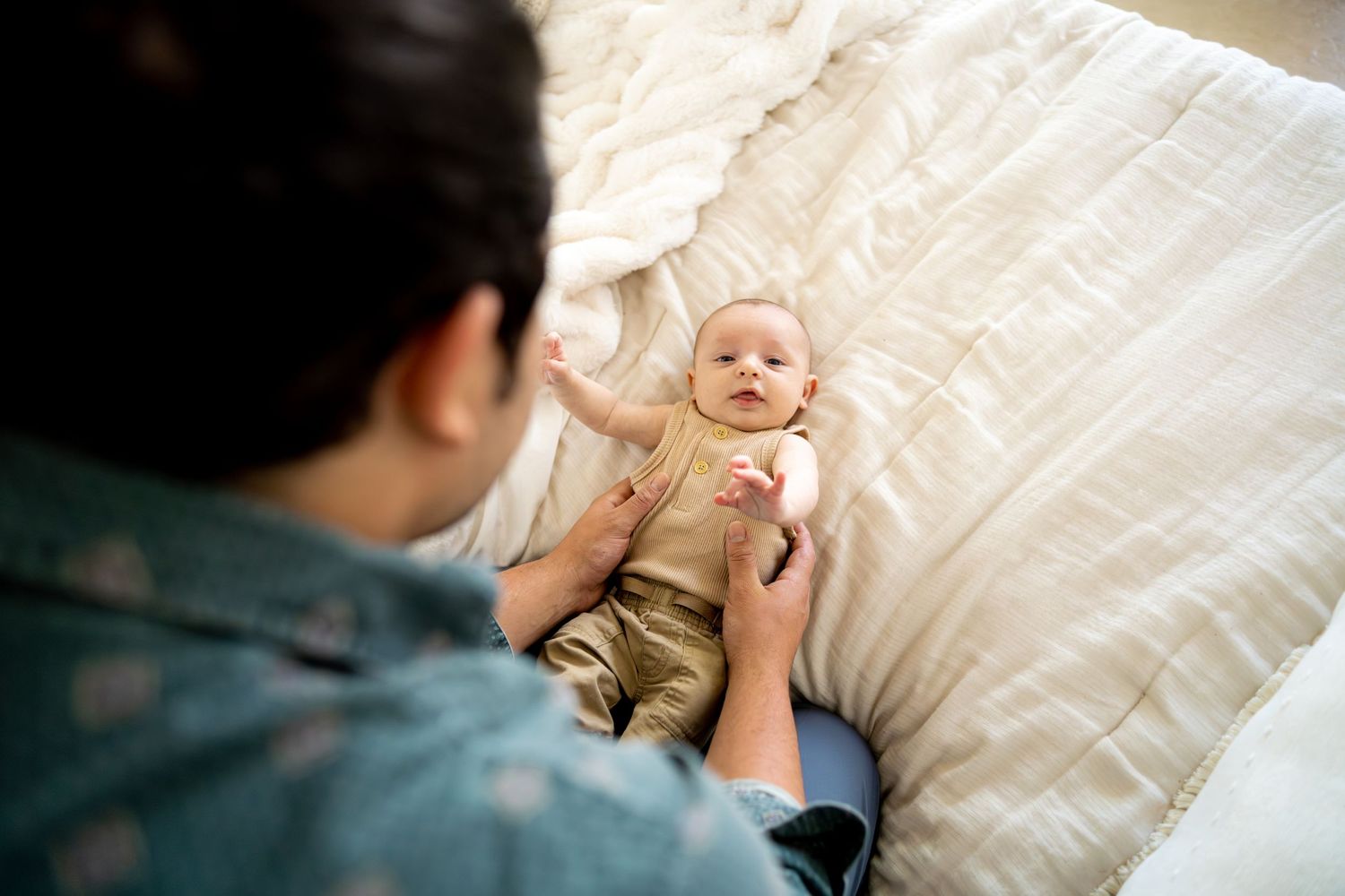 Parent and smiling baby share joyful moment together on white bedding.