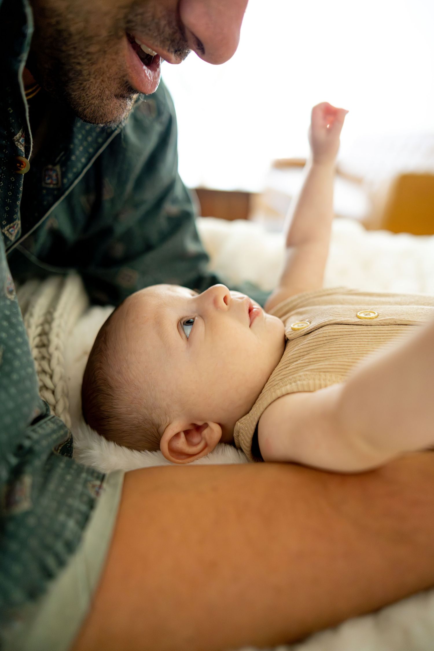 Parent leans in close to baby lying on couch during tender bonding moment.