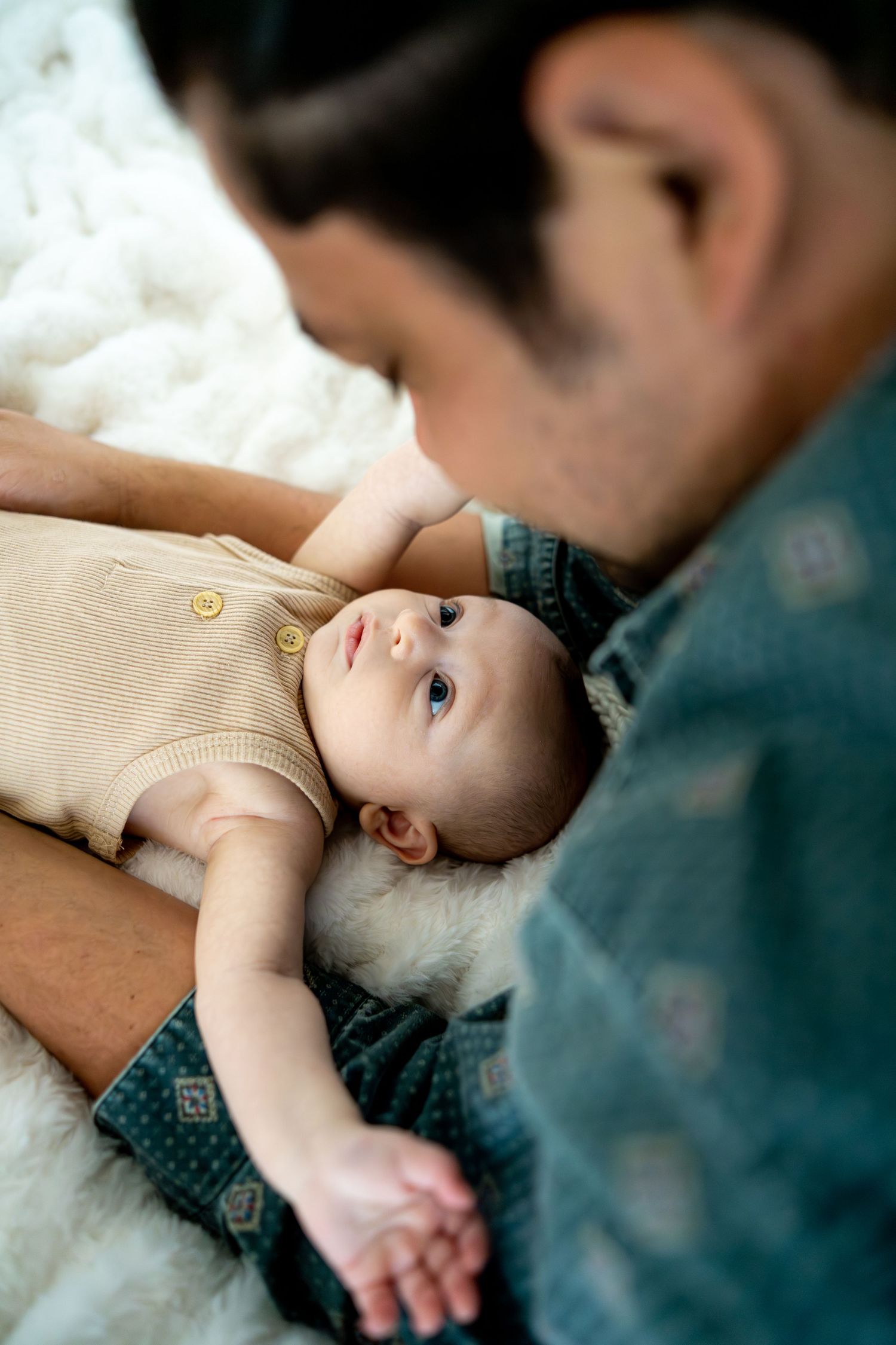 Close-up view of a baby in a beige onesie lying on white bedding.