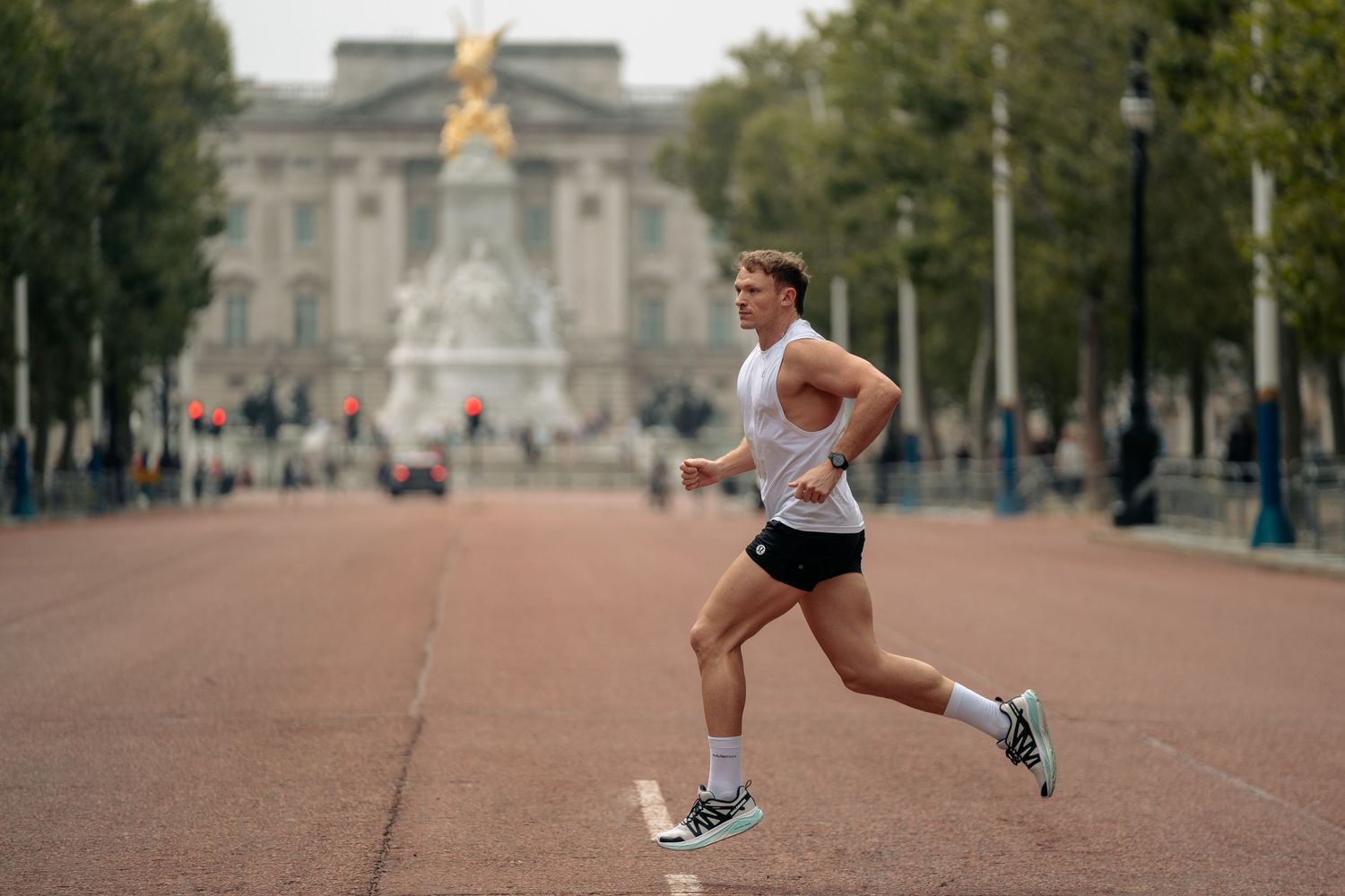 Runner in motion near Buckingham Palace with Victoria Memorial visible in background.