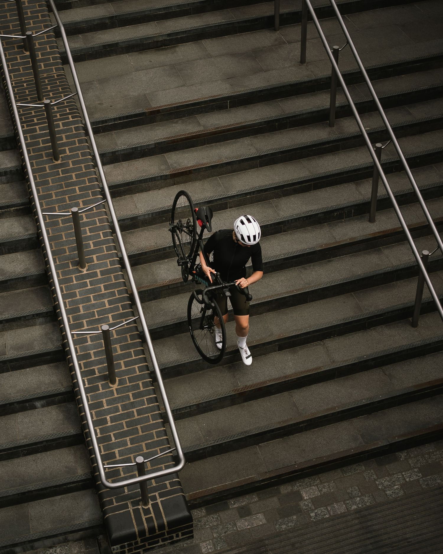 Cyclist carrying bike up concrete steps in dramatic overhead urban composition.