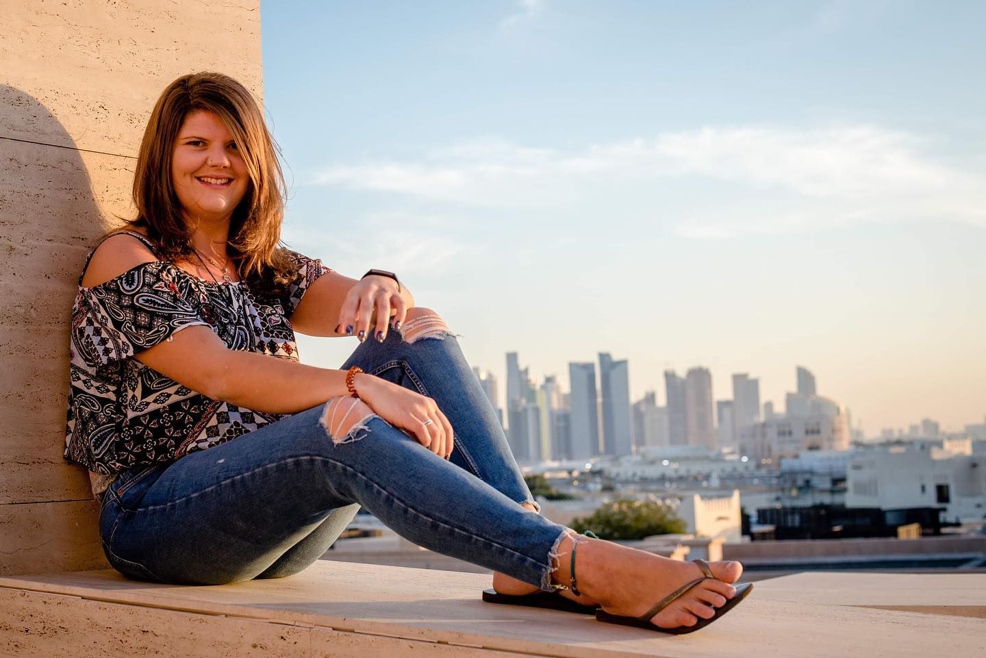 portrait of girl sat on a ledge with doha city in the background