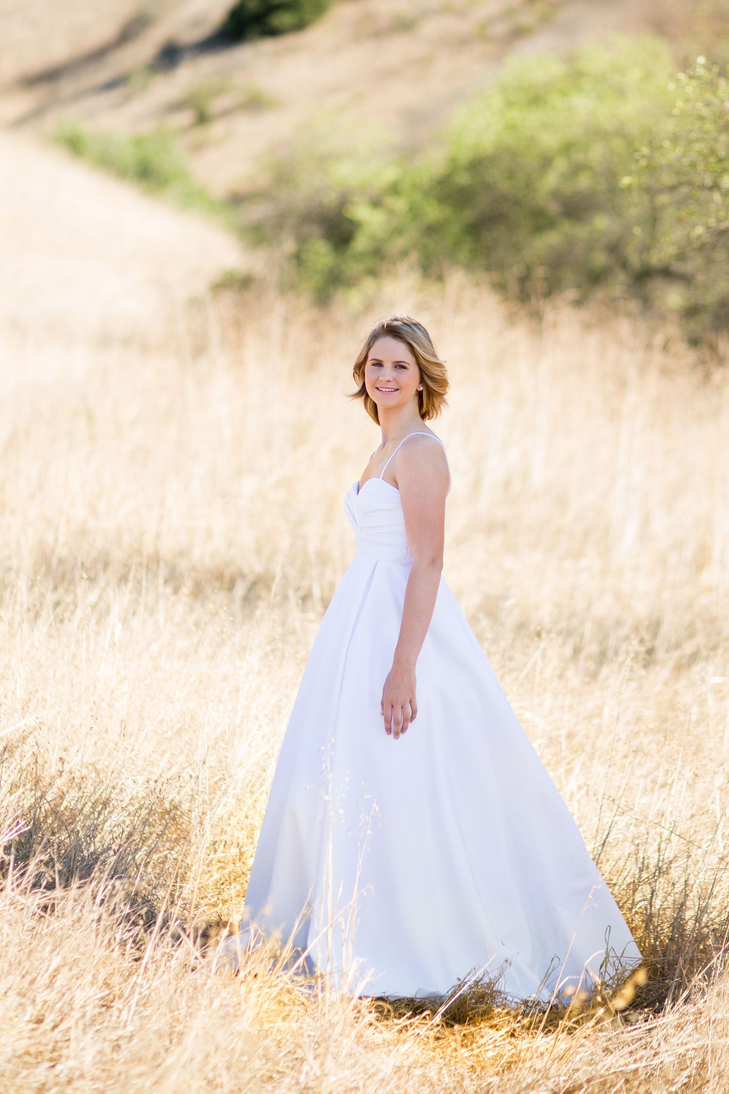 Ethereal bridal portrait in flowing white gown amid golden summer field.