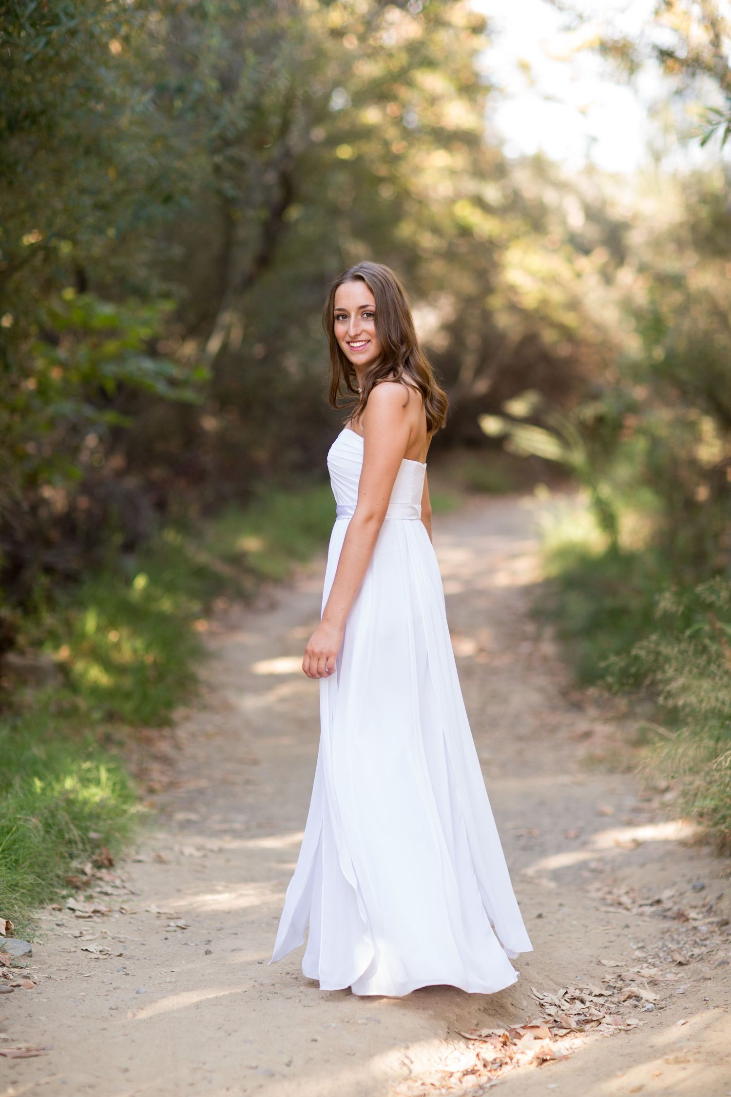 Elegant white dress portrait on natural forest path with dappled sunlight.