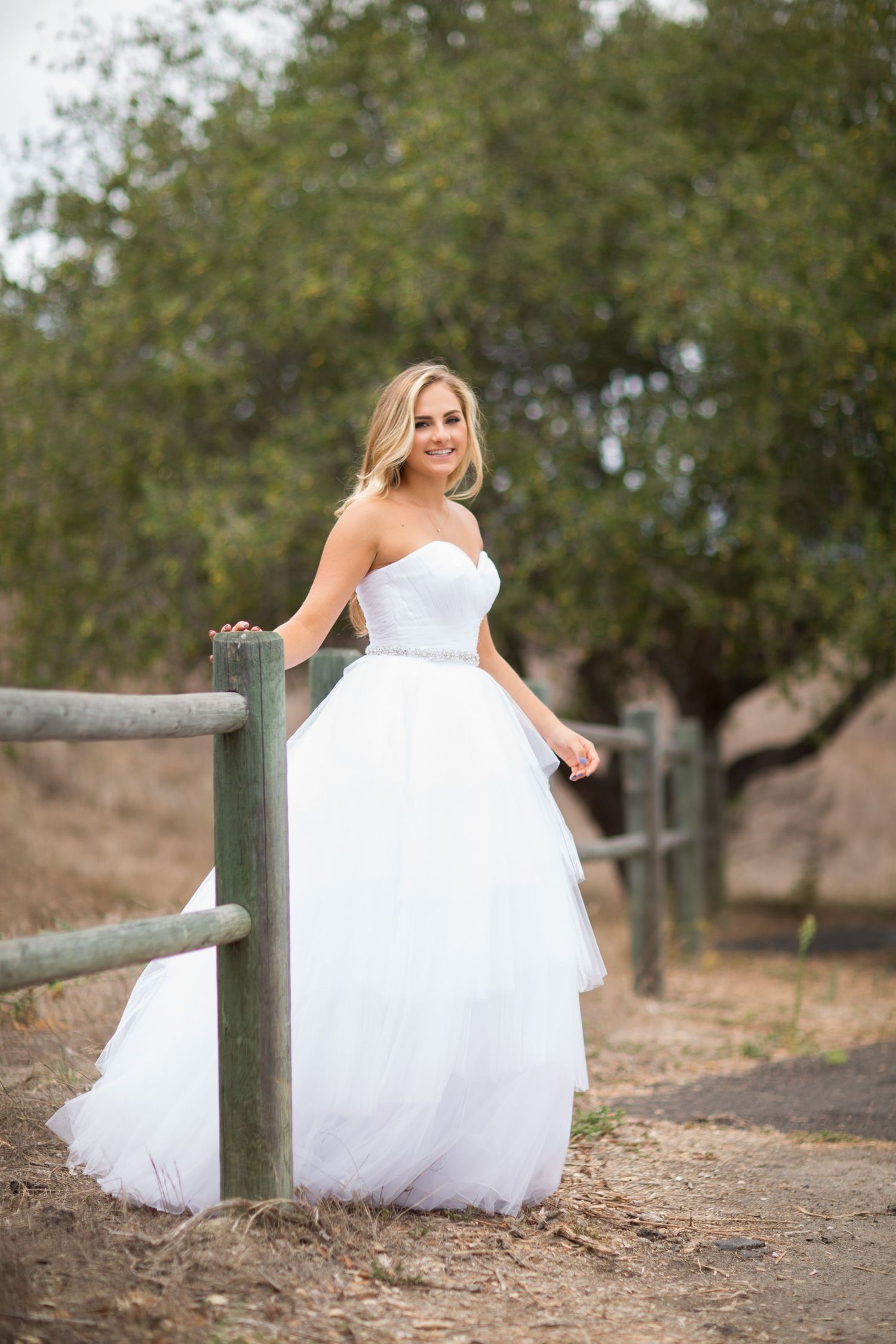 Romantic bridal photo with white ballgown dress near rustic wooden fence.