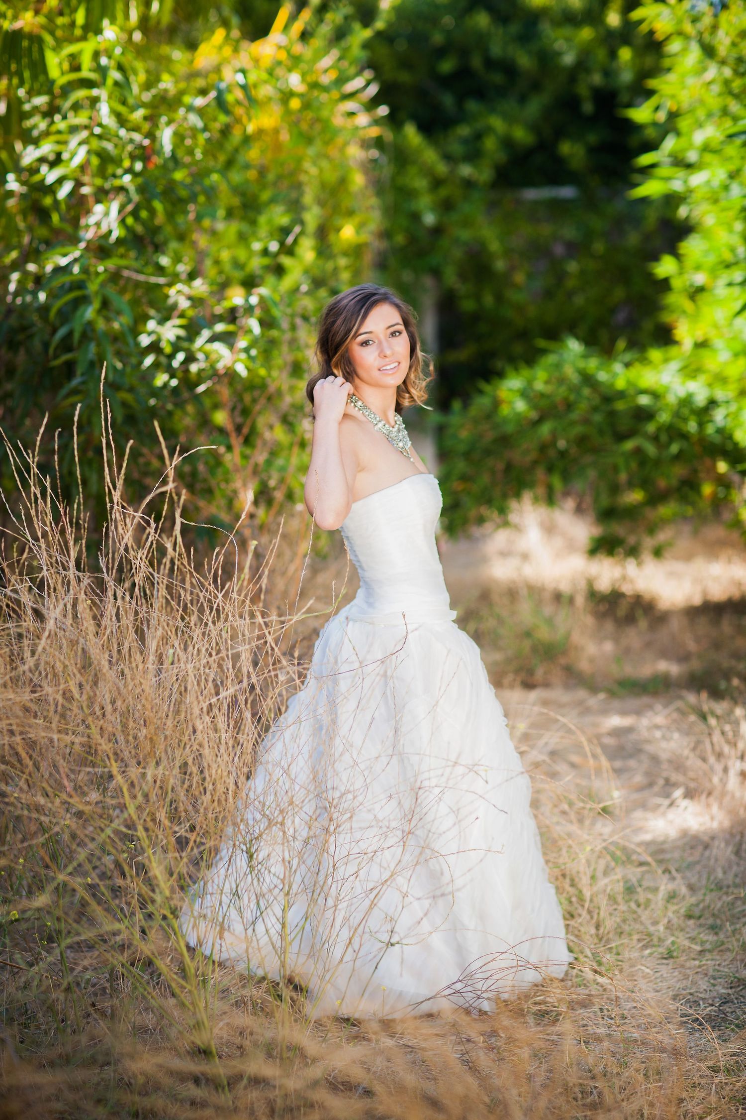 Romantic bridal portrait in a textured white gown amid tall grasses and greenery.