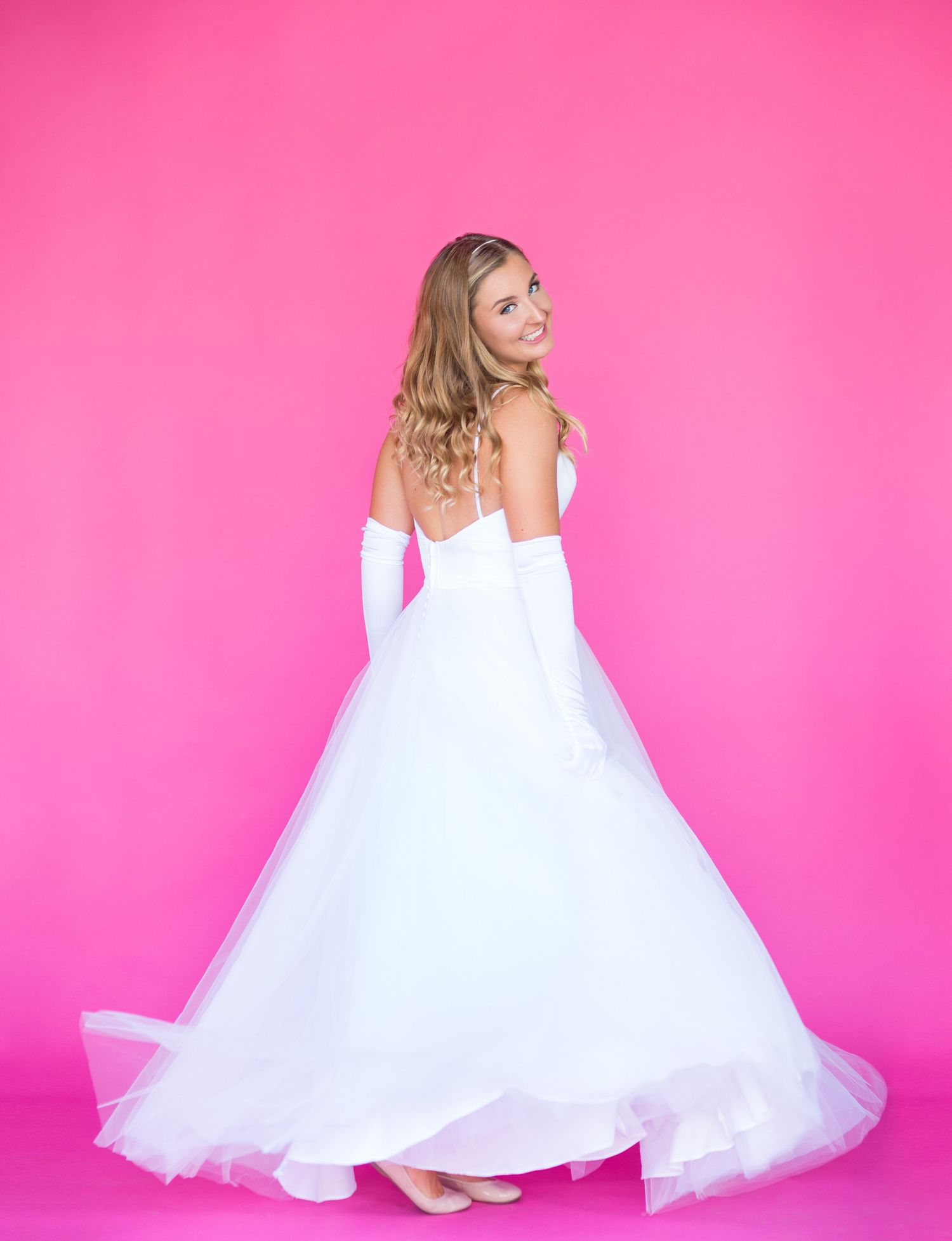 A princess style wedding dress twirls against a bright pink background.