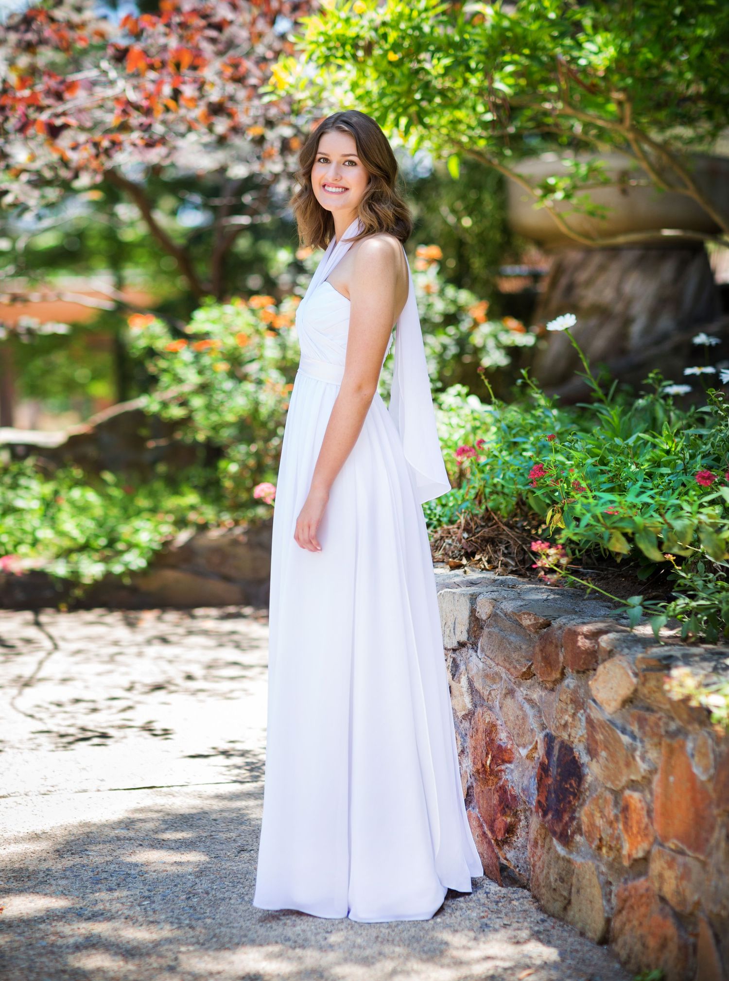A flowing white wedding dress photographed in a garden setting with stone walls.