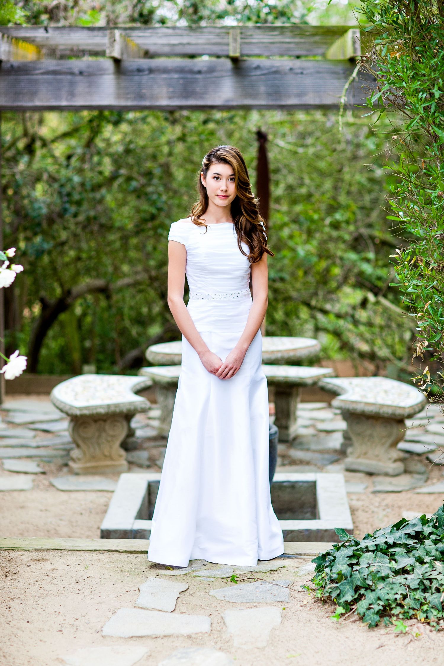 Classic white wedding dress portrait in garden setting with stone path and bridge.