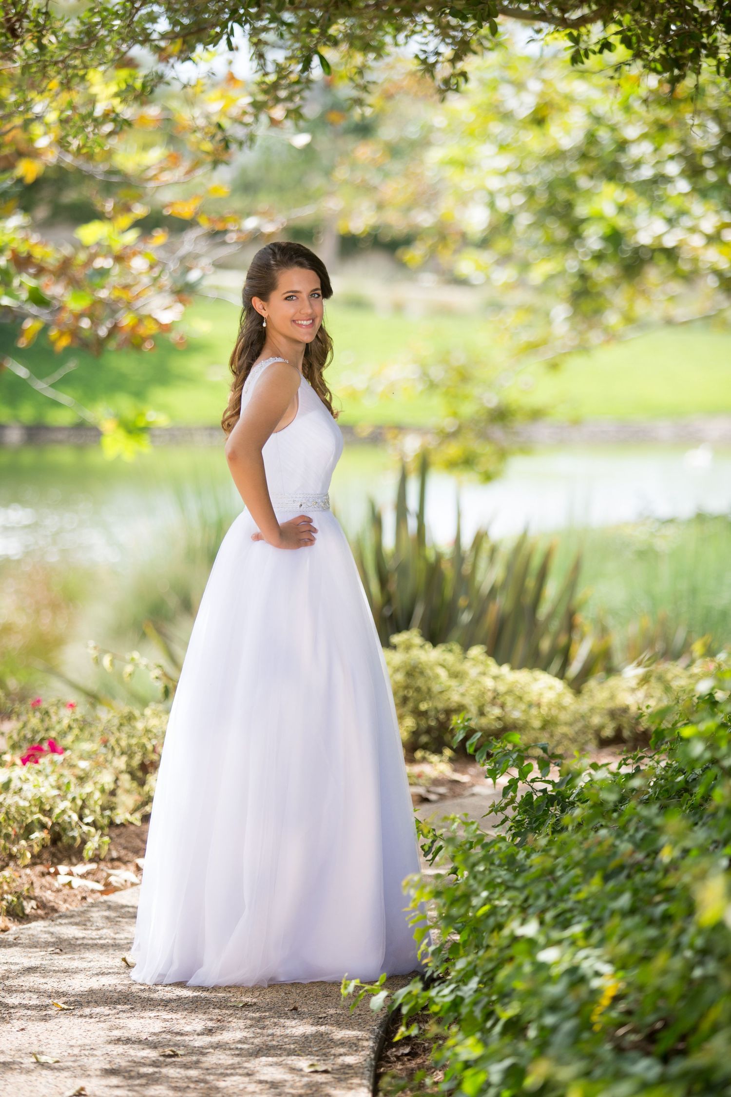Classic bridal portrait in white gown by serene garden pond with lush greenery.