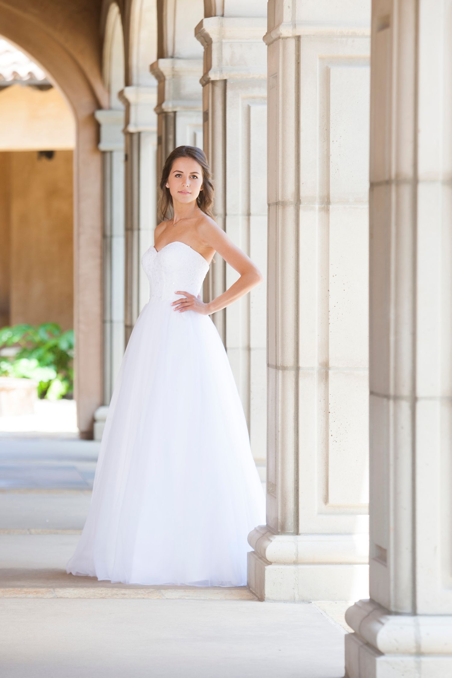 Elegant bridal portrait under stone archways featuring a strapless white wedding gown.