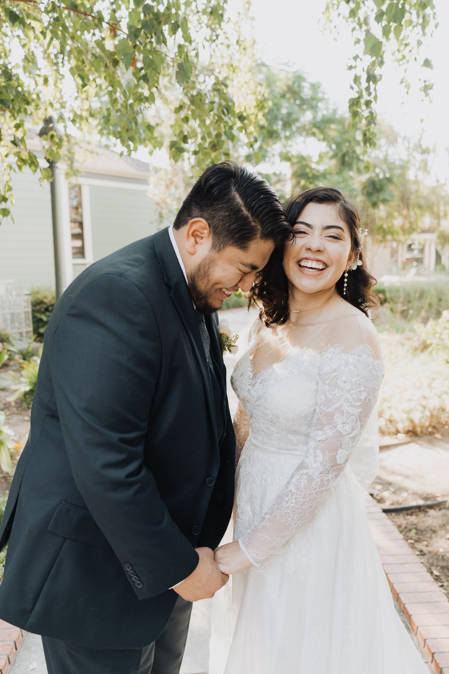 Wedding couple sharing an intimate moment in a garden setting with lace dress and black suit.