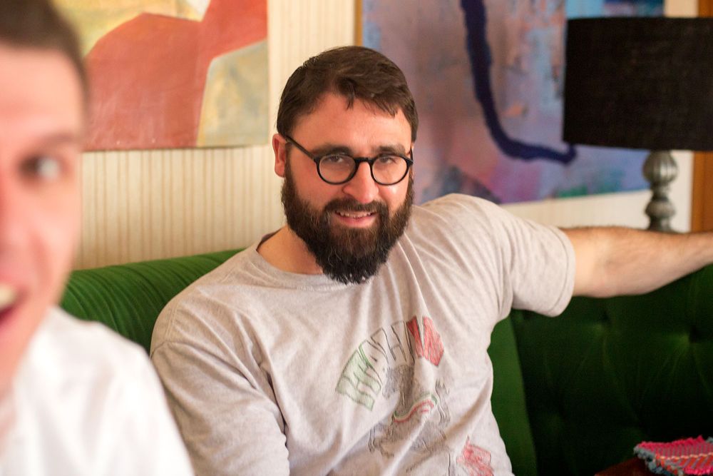Man in glasses and casual attire relaxing on green couch in casual setting.