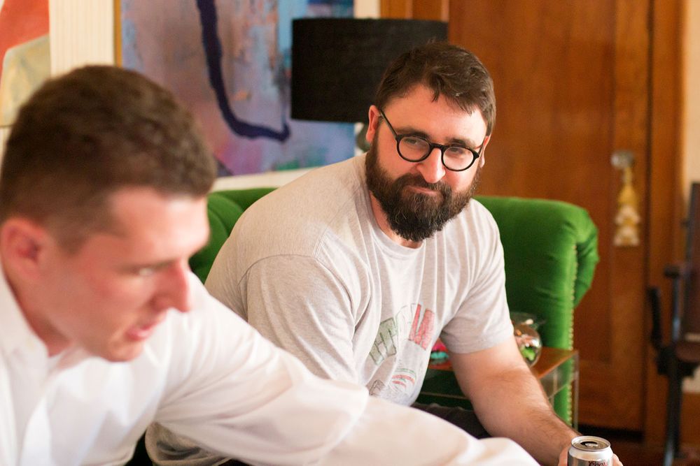 Two men having a conversation while seated on green furniture indoors.