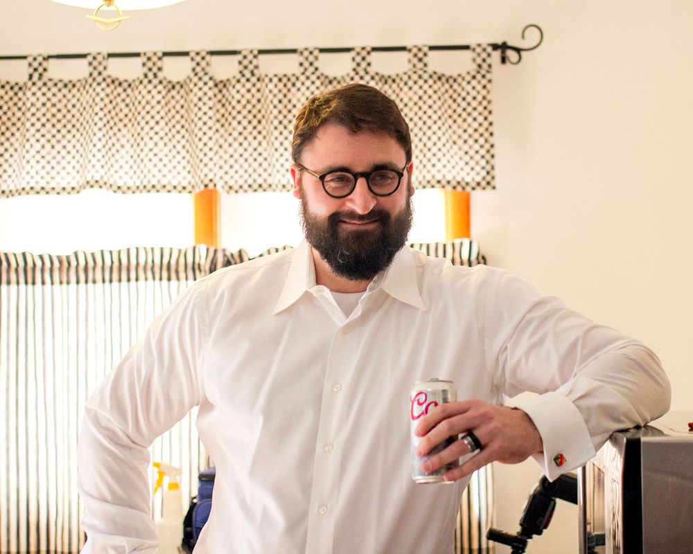 Man in white shirt and glasses holding playing cards in front of decorative curtains.