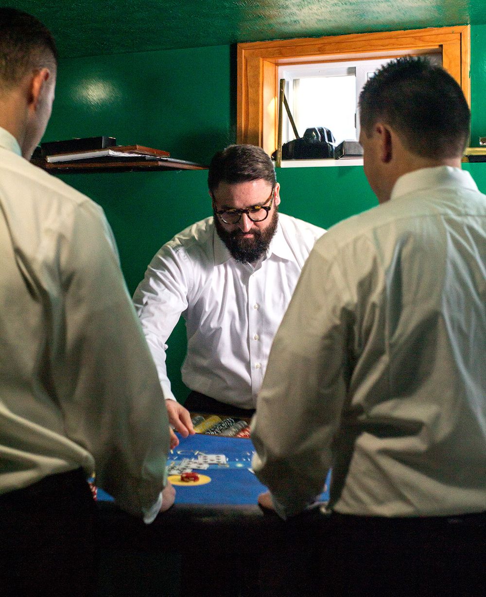 Group gathered around gaming table wearing white shirts in green-walled room.