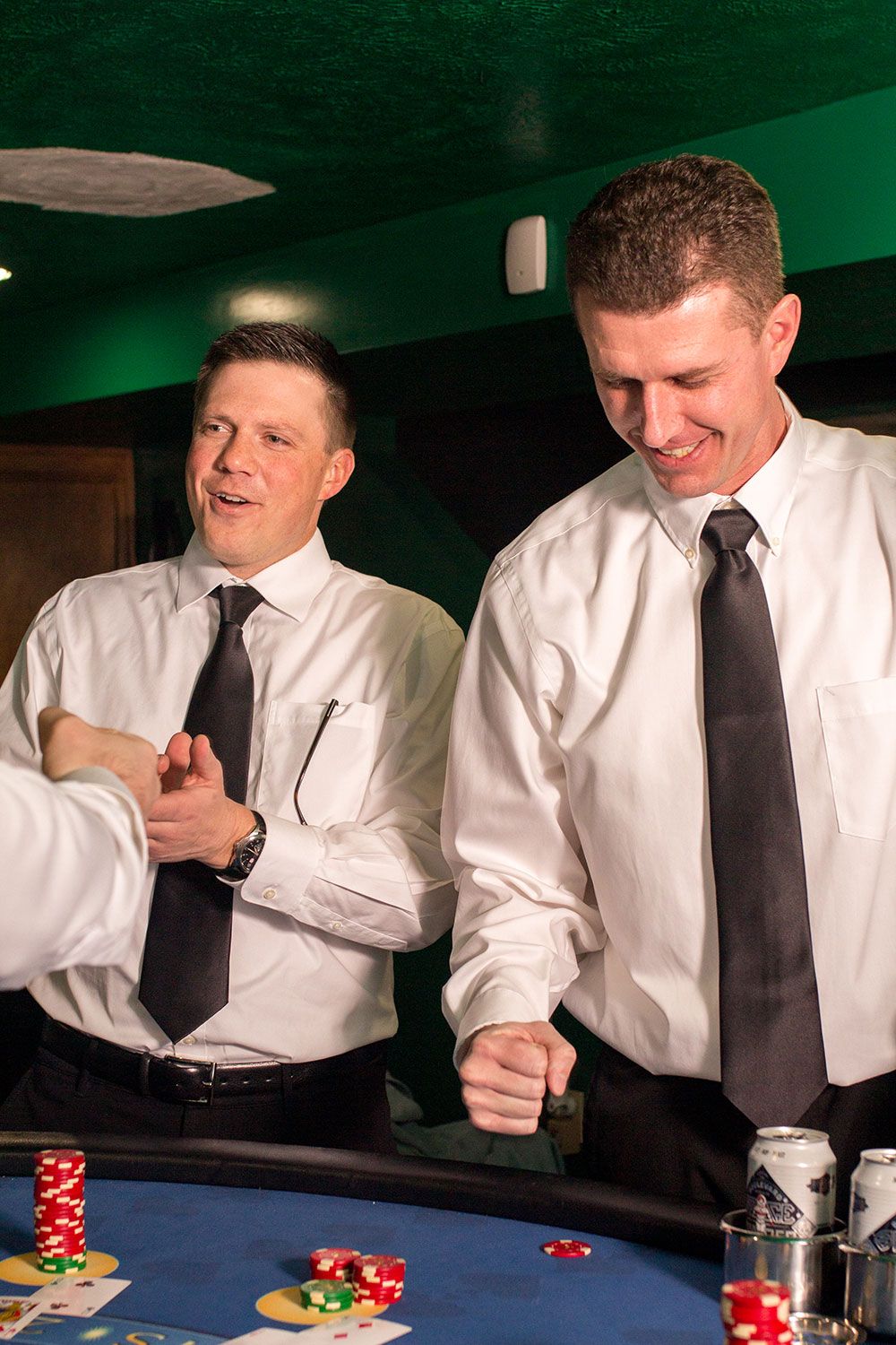 Players in white shirts and black ties gather around a casino table placing bets.