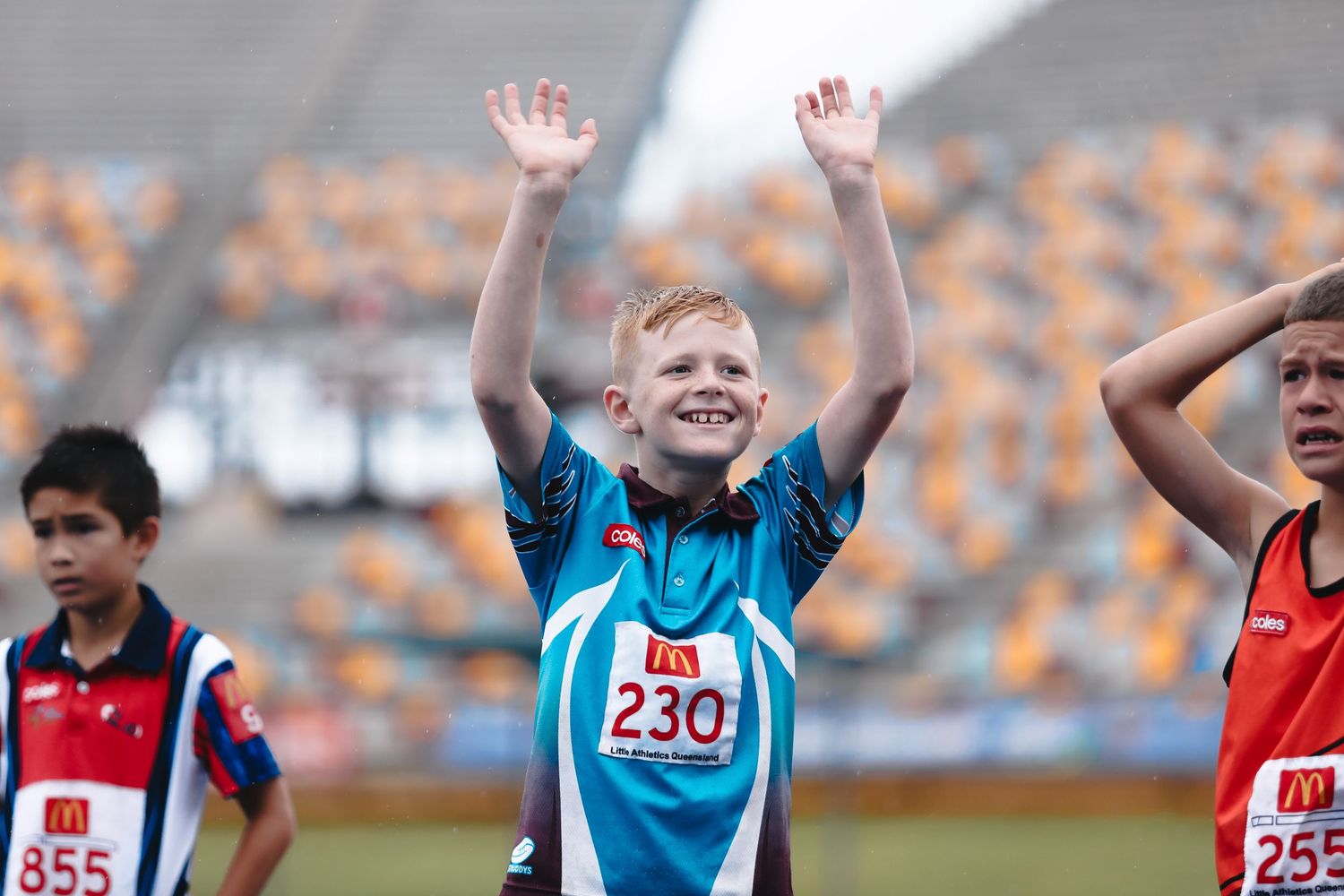 Young athlete celebrates with raised arms at track and field event.