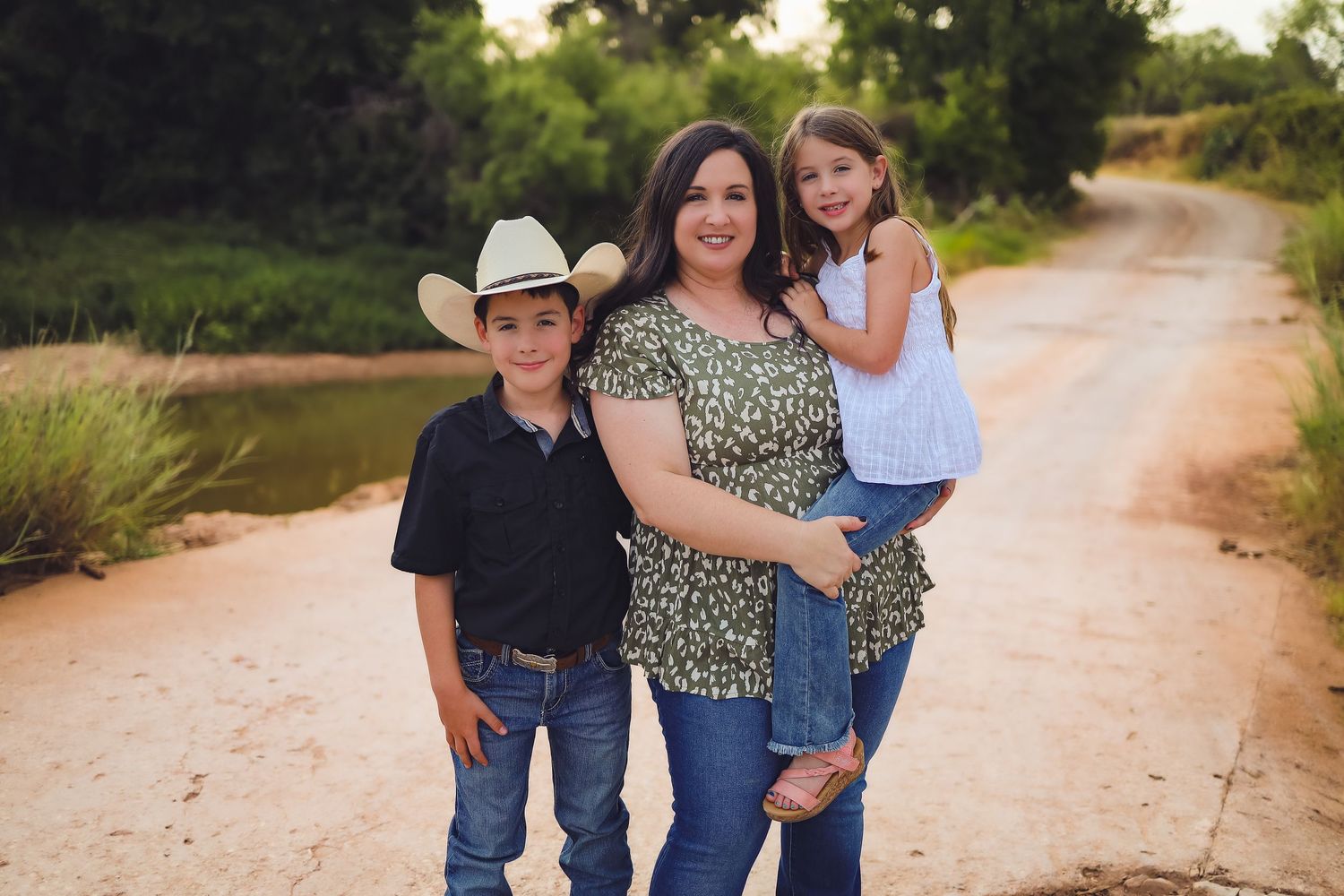 A family in casual western attire poses together on a dirt road during golden hour.