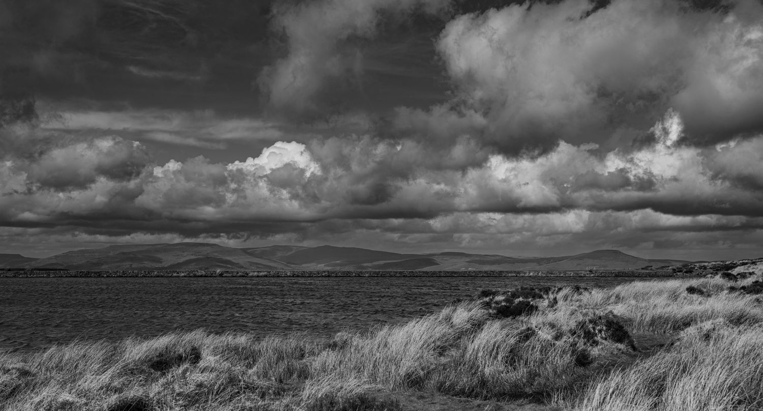 Dramatic black and white landscape of rolling hills under stormy skies with billowing clouds.