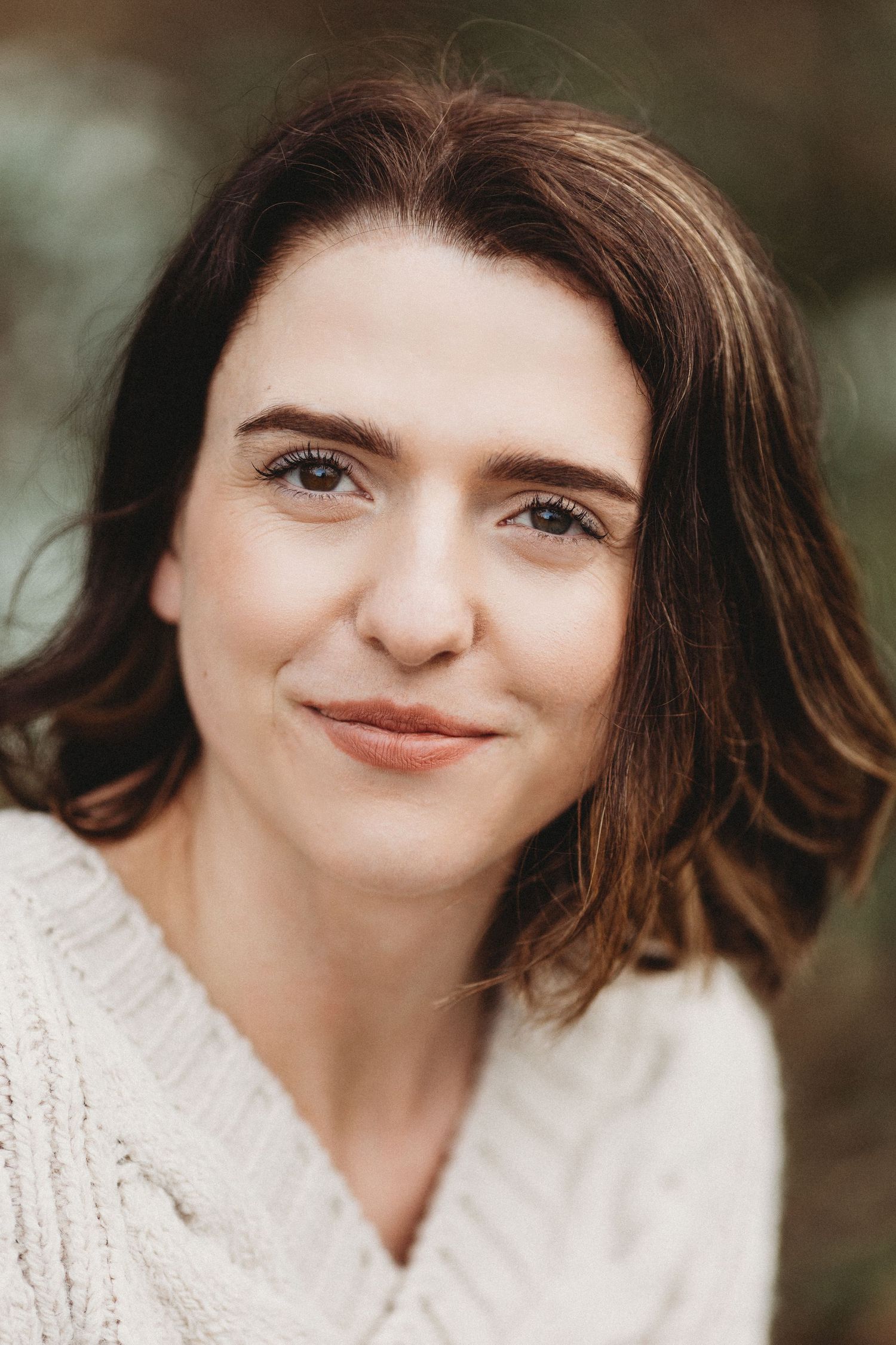 Portrait of person in cream sweater with short brown hair smiling at camera.