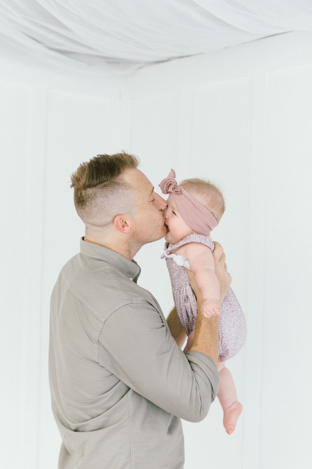 Tender moment between parent and baby in pink dress against white backdrop.
