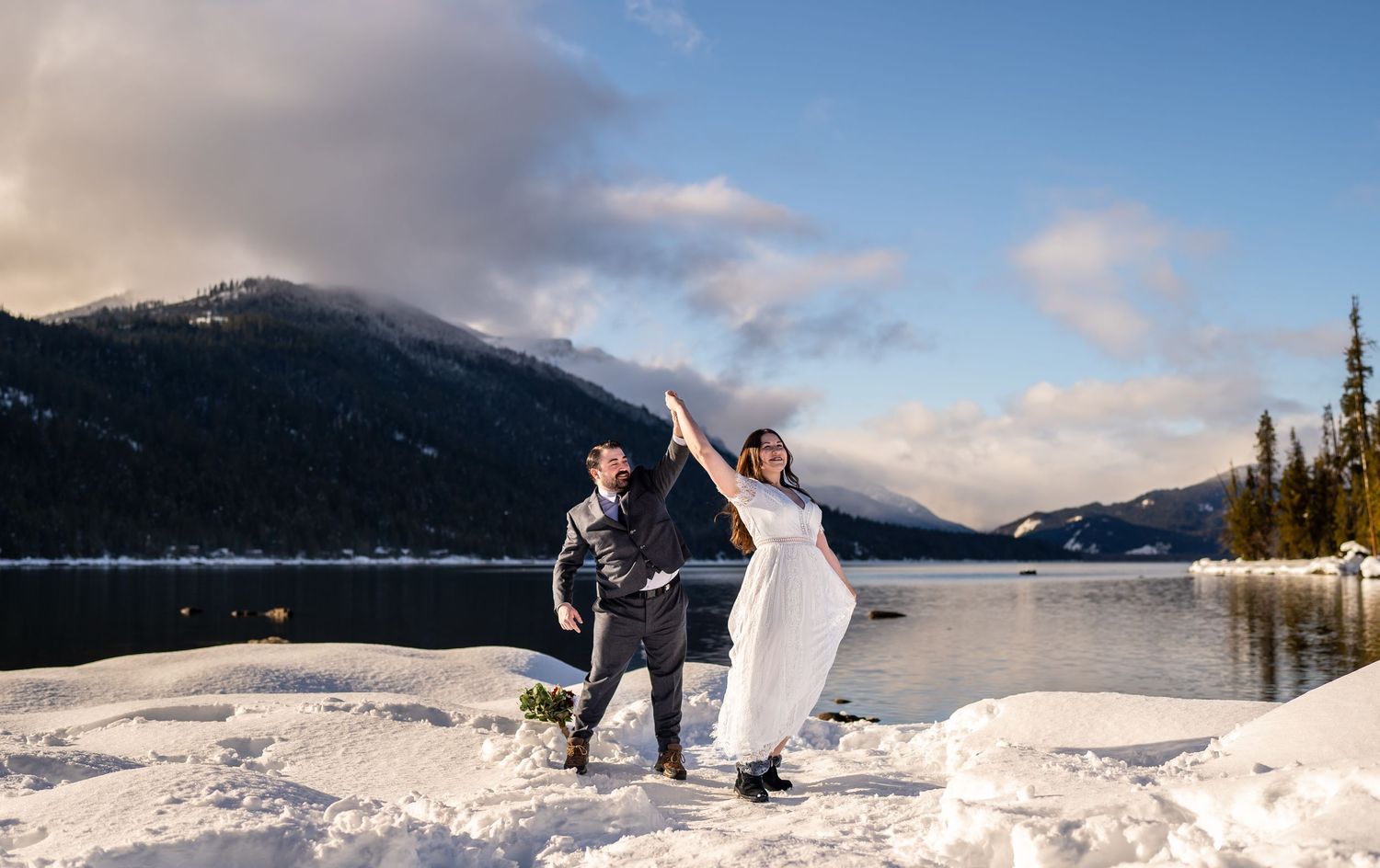 Couple celebrating during their winter wedding ceremony by a snow-covered mountain lake.