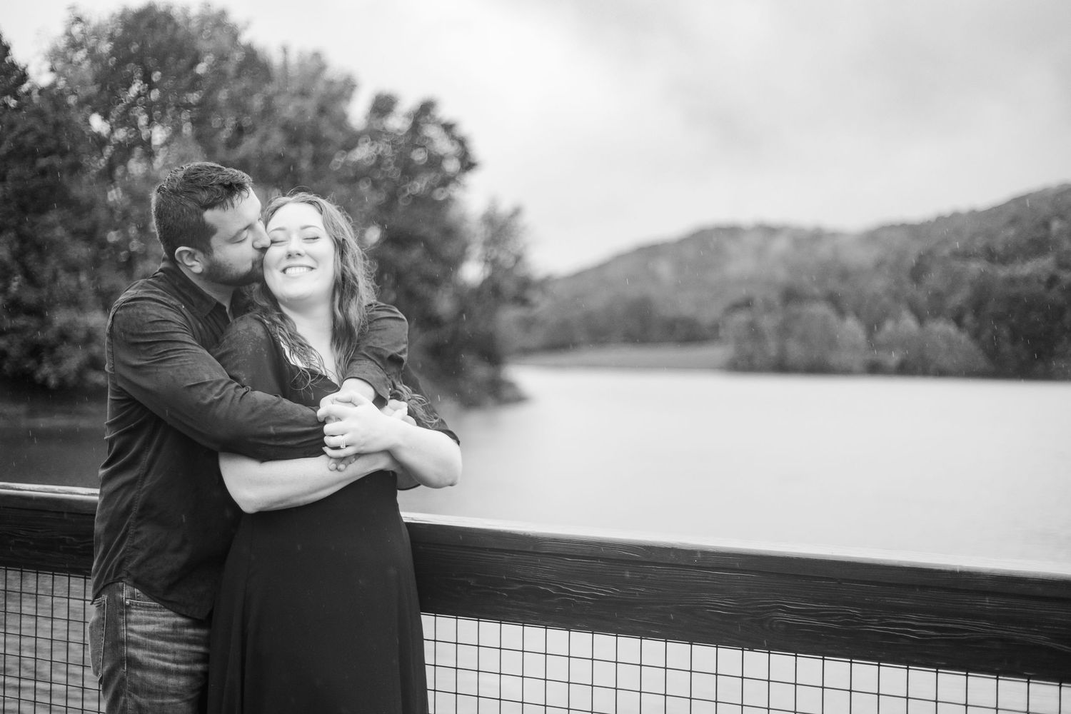 A couple embraces on a lakeside overlook during an outdoor photoshoot.
