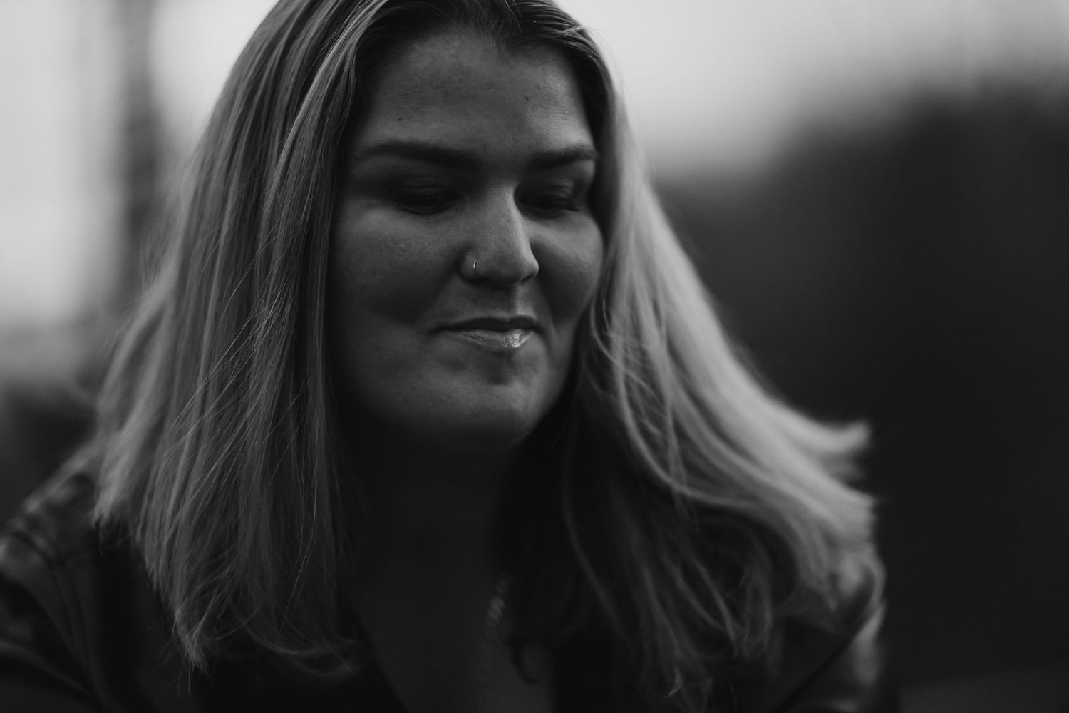 A black and white portrait with a gentle smile and windswept hair against a blurred background.