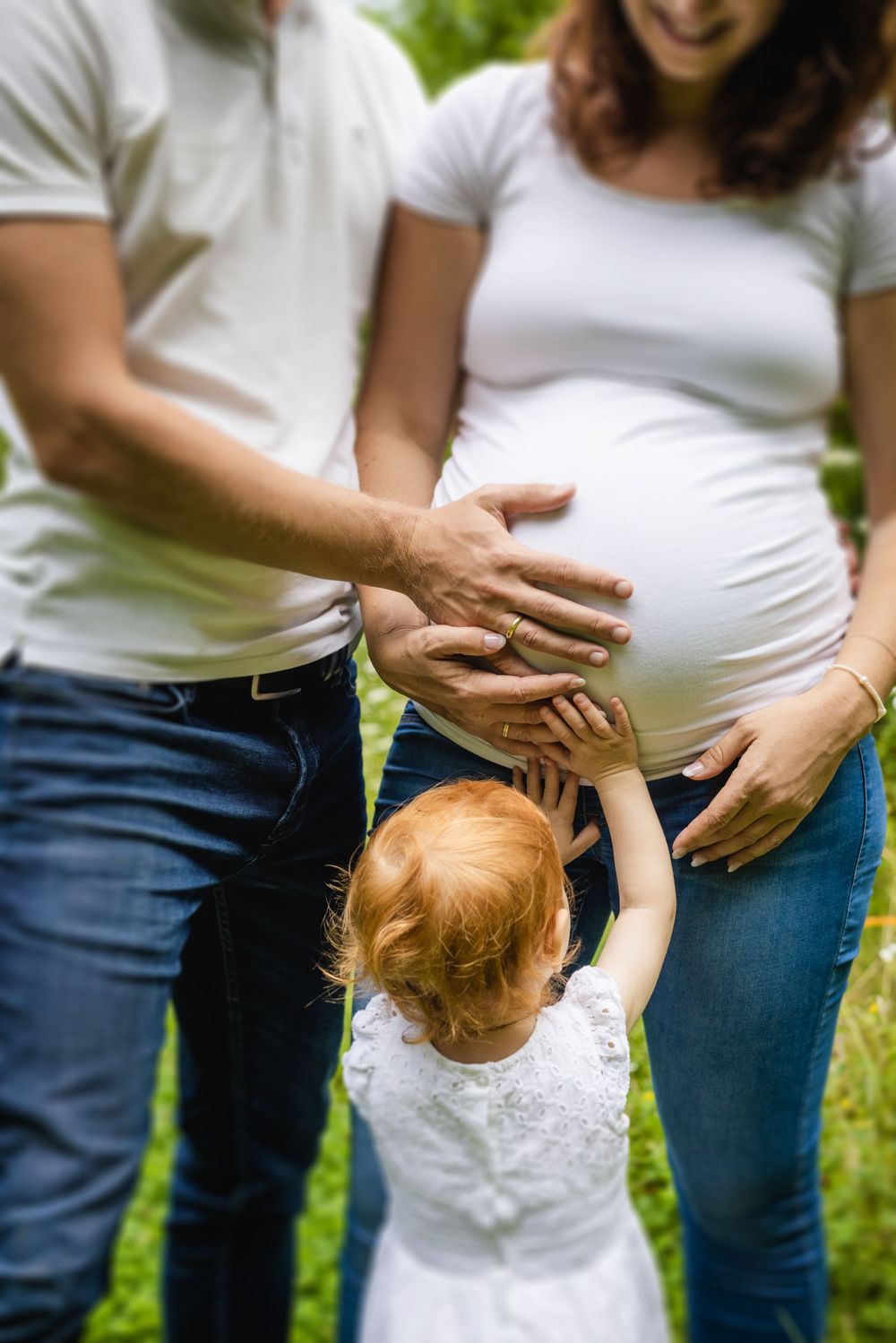 Close up of family hands touching pregnant belly in garden setting.