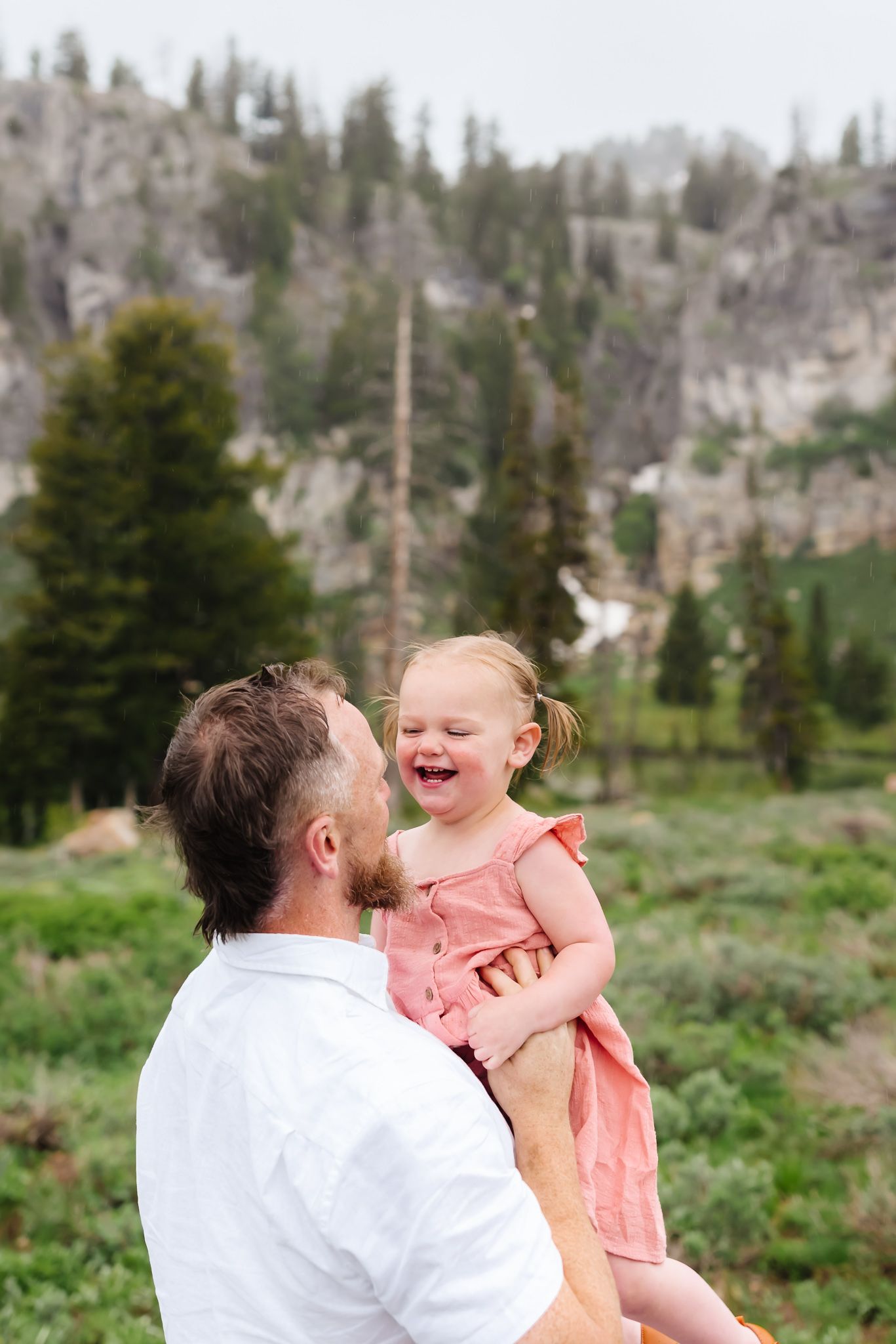 Joyful outdoor family moment in a mountain meadow with evergreen trees in the background.