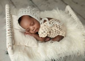 Sleeping newborn in white knit wrap on white fur bed.
