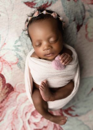 Peaceful sleeping newborn wearing floral crown and wrapped in soft pink swaddle.