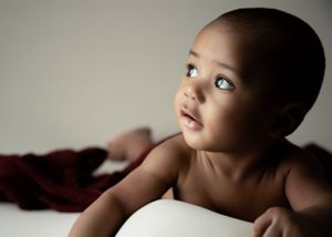 Baby posing on white surface with maroon blanket in artistic portrait.